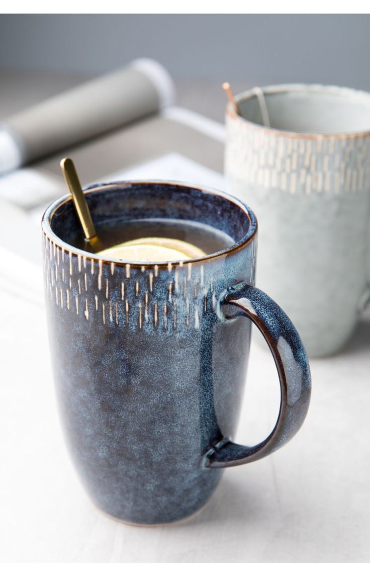 two coffee mugs sitting next to each other on a table with writing utensils