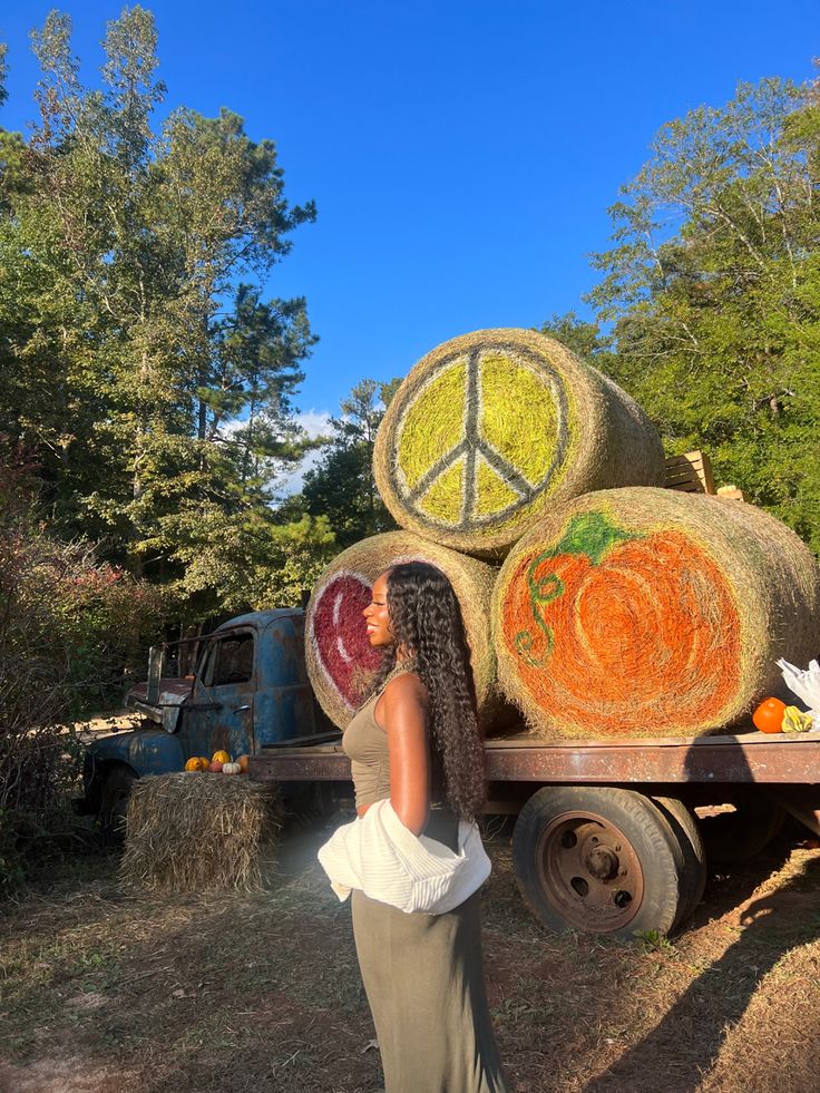 a woman standing in front of a truck with hay bales and pumpkins on it