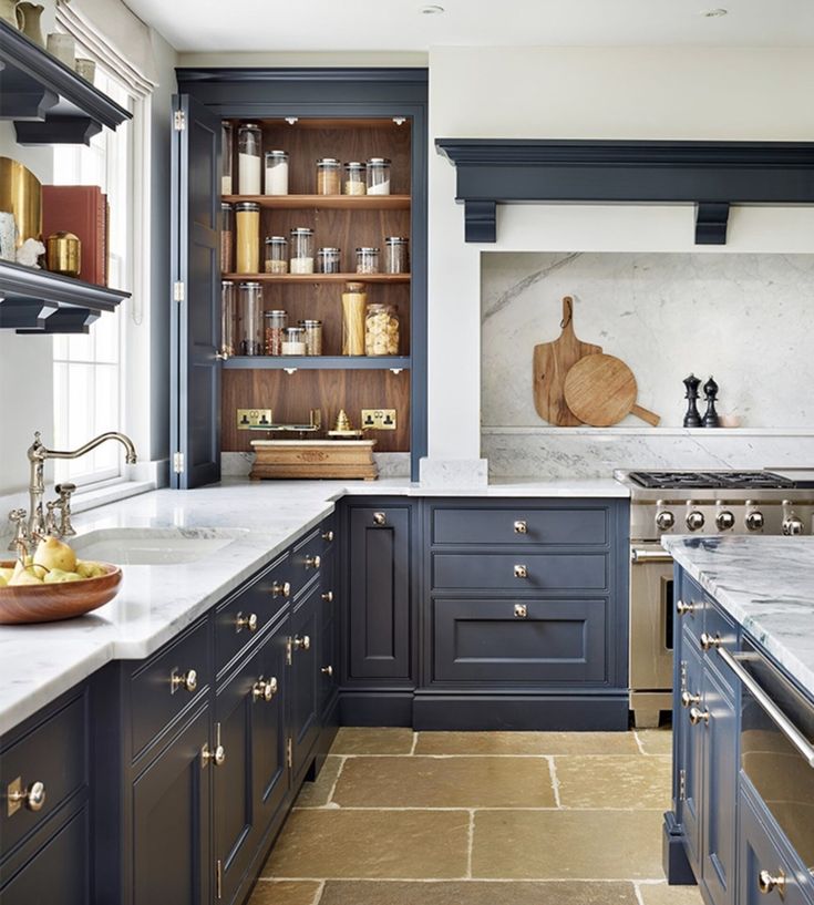 a kitchen with marble counter tops and blue cabinets, along with brass pulls on the doors