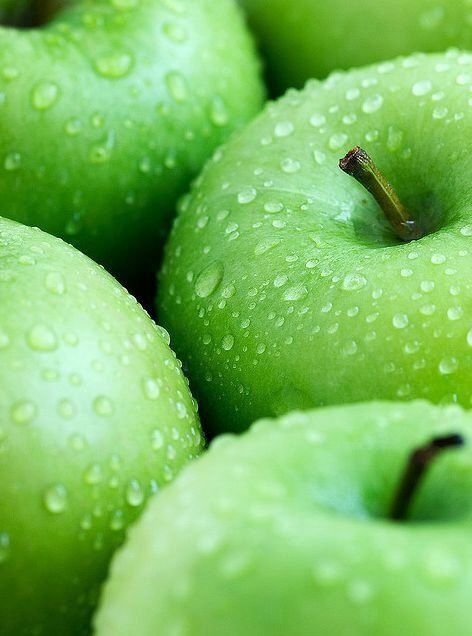 green apples with water droplets on them are stacked together in a pile, ready to be eaten