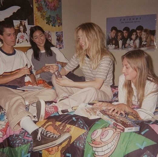 four people sitting on a bed with one woman looking at her phone and the other smiling