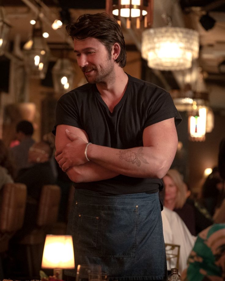 a man with his arms crossed standing in front of a table full of people at a restaurant