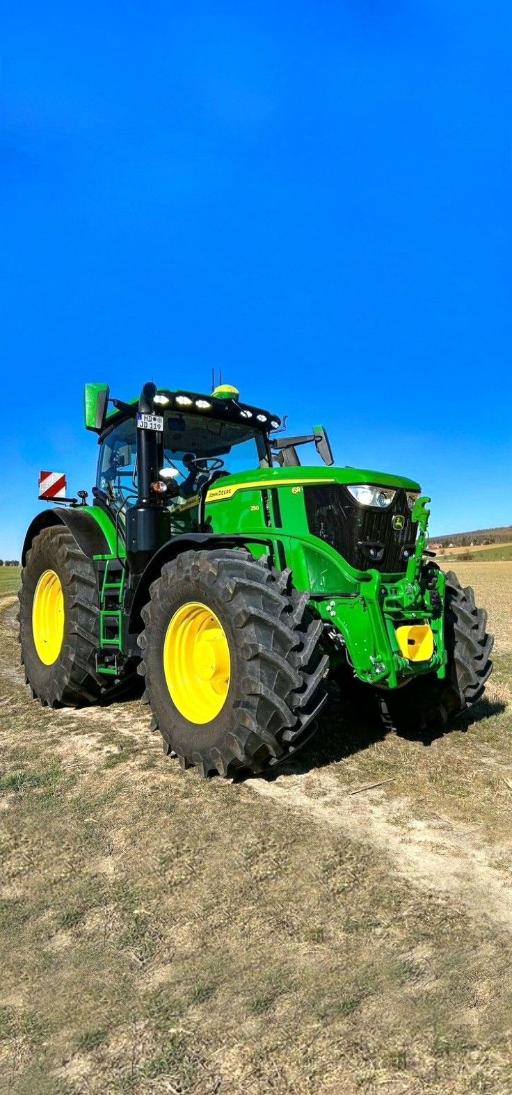 a large green tractor parked on top of a dry grass field next to a blue sky