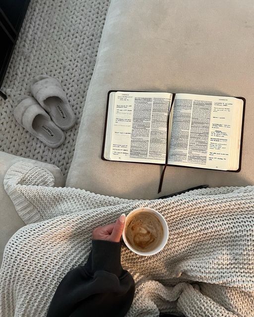 someone is reading a book and holding a cup of coffee while laying on the couch