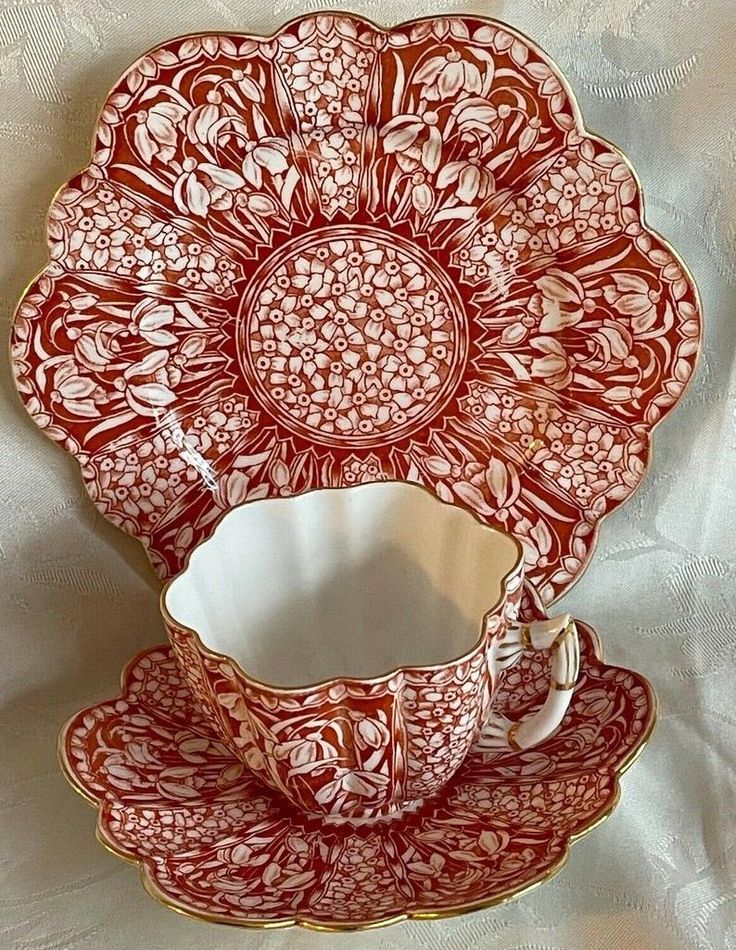 an ornately decorated red and white tea cup and saucer set on a white tablecloth