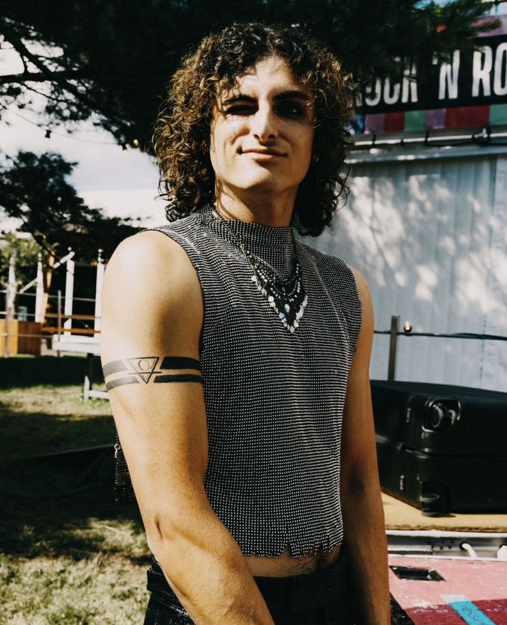 a man with long hair and tattoos standing in front of a train