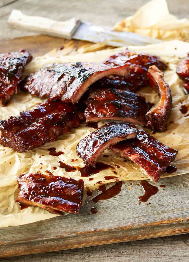 barbecue ribs on a cutting board next to a knife and some other meats that have been marinated