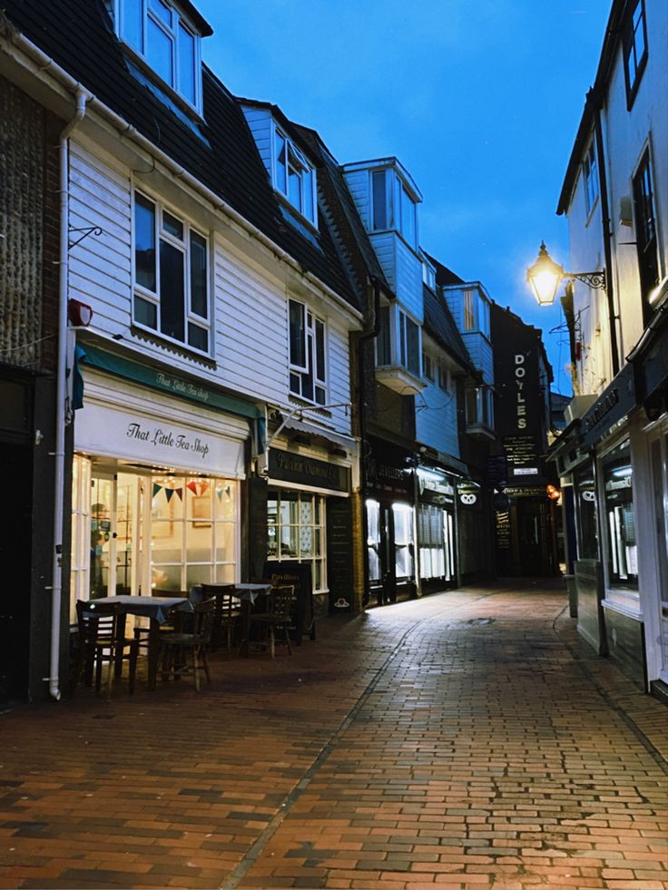 a cobblestone street lined with shops and restaurants at dusk in an old european town