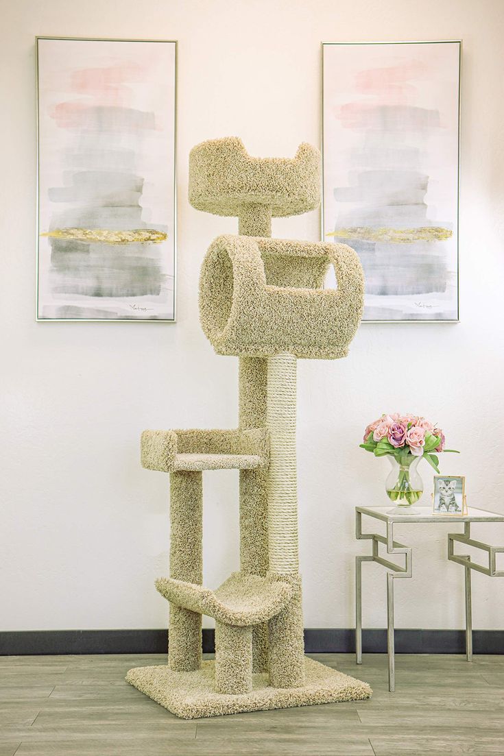 a cat tree in the middle of a room with two paintings on the wall behind it