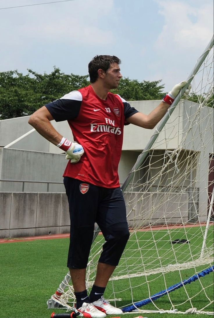 a man standing in front of a soccer goal holding a ball and glove on his hand