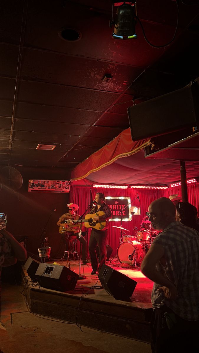 the band is playing in the dark with red light coming from behind them and people standing around