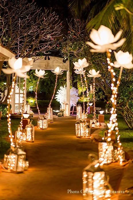 lighted lanterns are lined up on the path to an outdoor ceremony venue at night time