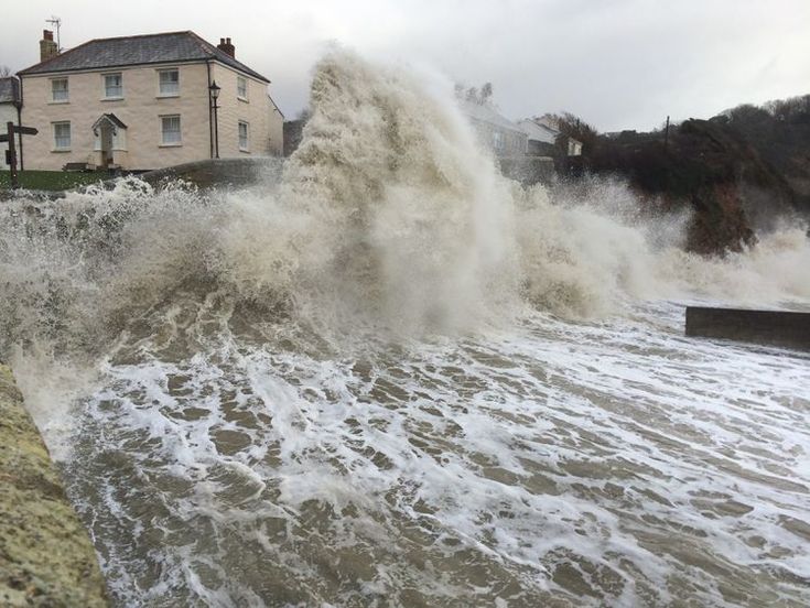 a large wave crashing into the shore next to a house