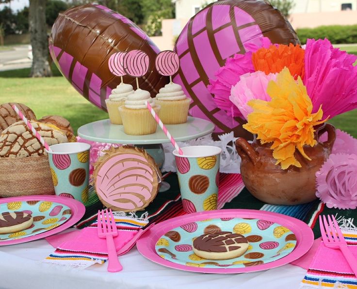 a table topped with plates and cupcakes next to a vase filled with flowers