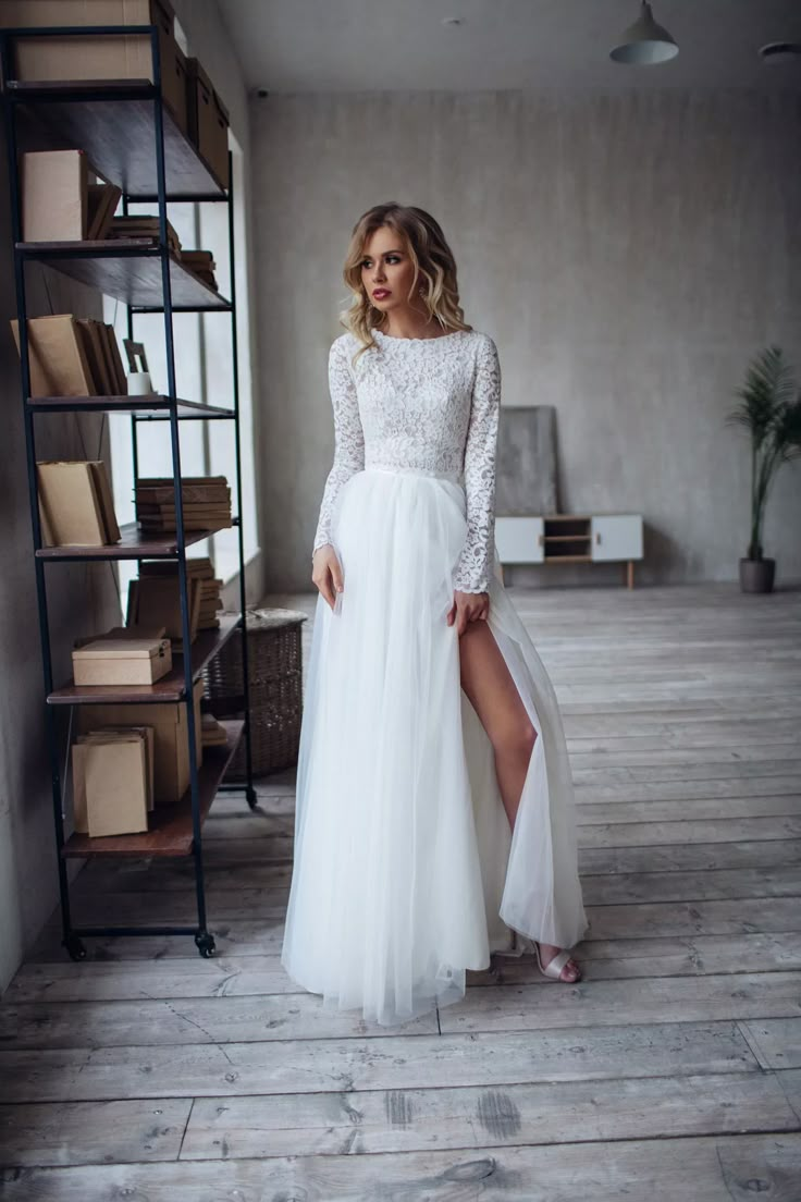 a woman in a white dress standing on a wooden floor next to a book shelf