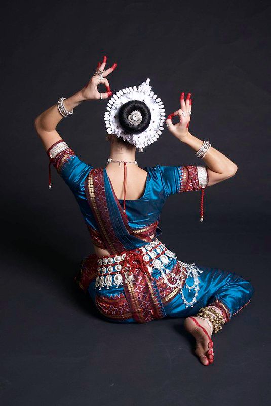 a woman in a blue dress and hat sitting on the floor with her hands up