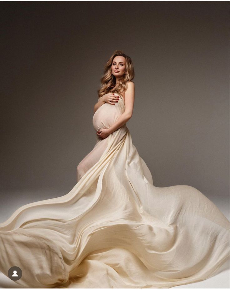 a pregnant woman in a flowing dress poses for a photo shoot with her belly exposed