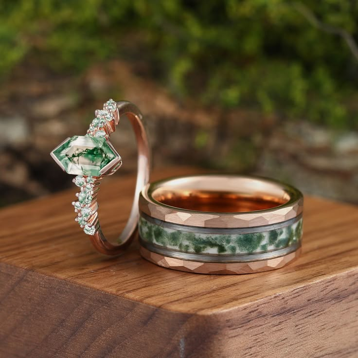 two wedding rings with green and white stones on top of each other sitting on a wooden surface