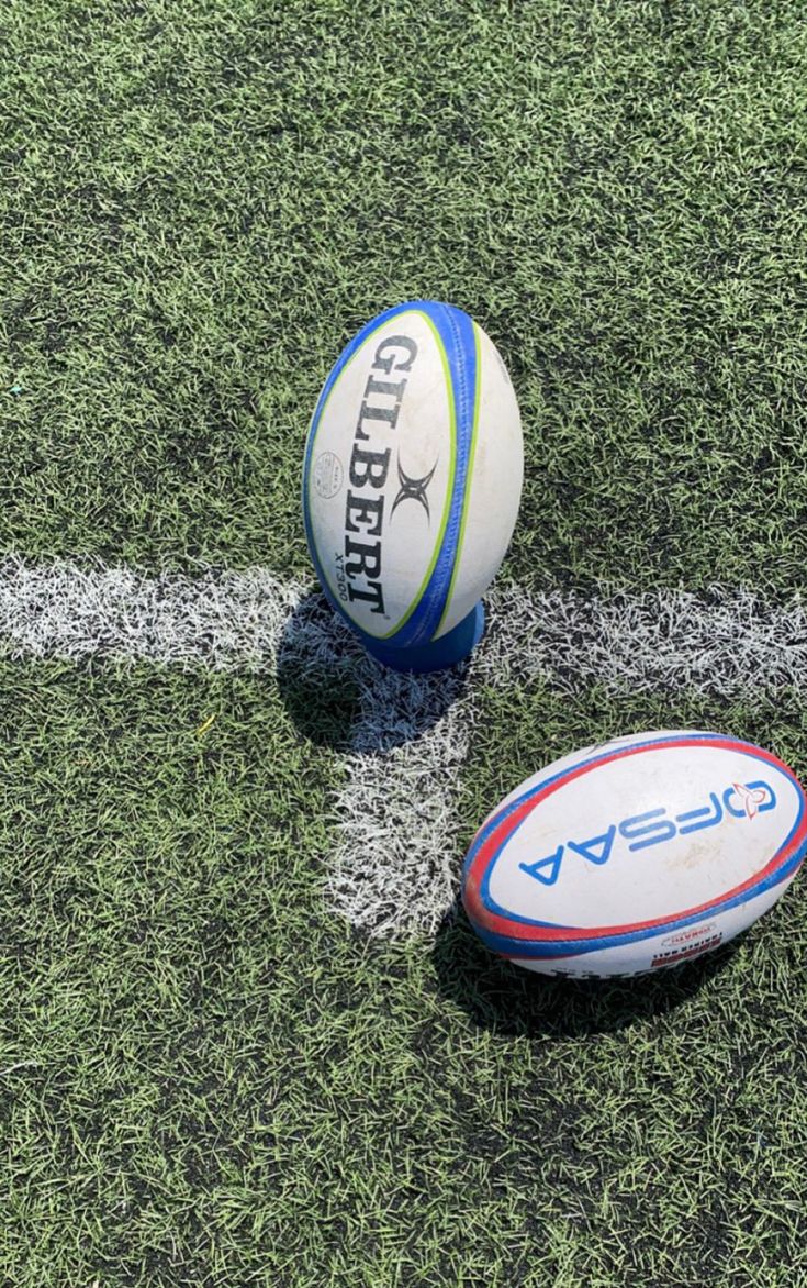 two rugby balls sitting on top of a field