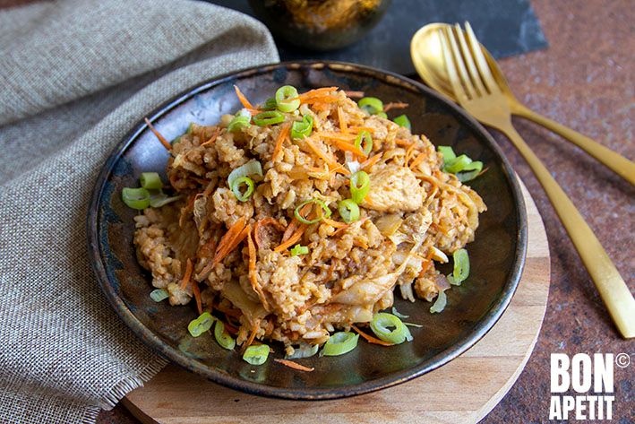 a black plate topped with rice and vegetables next to a silver fork on top of a wooden cutting board