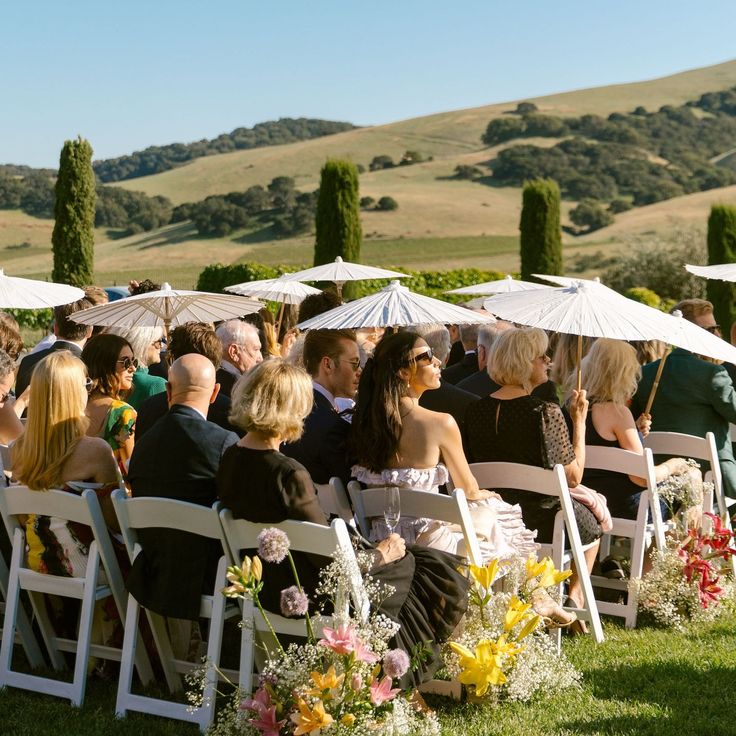 a group of people sitting under umbrellas on top of a grass covered field next to each other