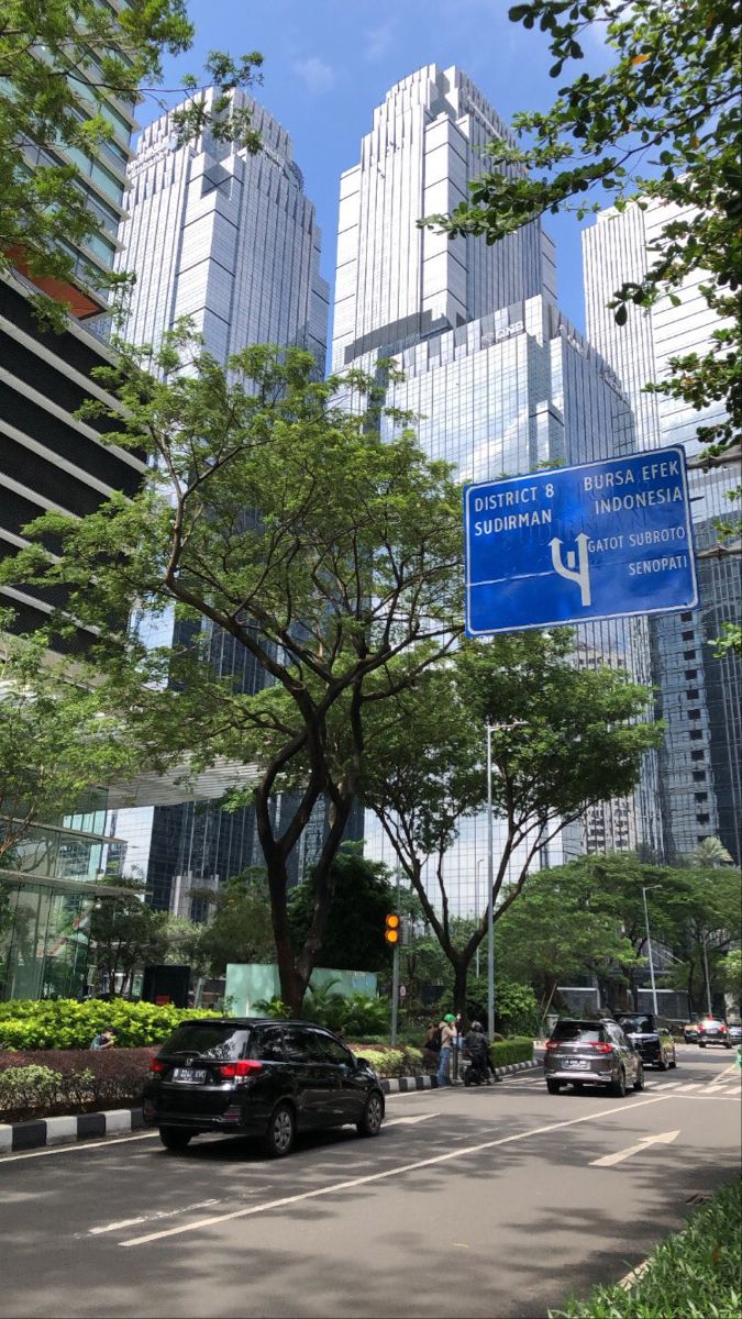 cars are driving down the street in front of tall buildings and skyscrapers on a sunny day