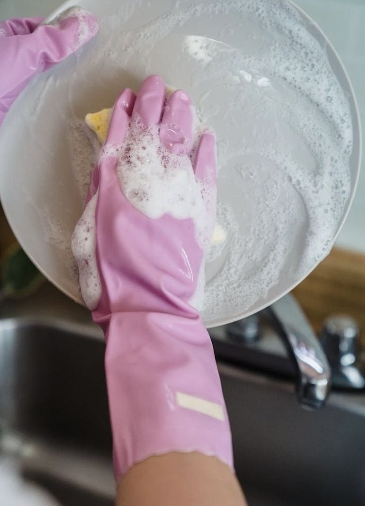 a person in pink gloves is washing dishes with soap and sponges on their hands