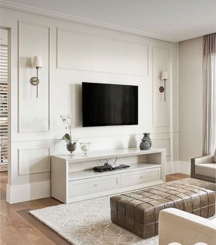 a living room with white furniture and a flat screen tv mounted on the wall above it