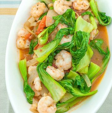 a white bowl filled with shrimp and veggies on top of a striped table cloth