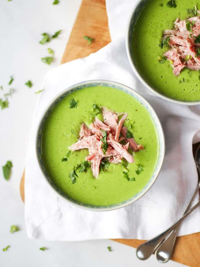 two bowls filled with green soup on top of a wooden table