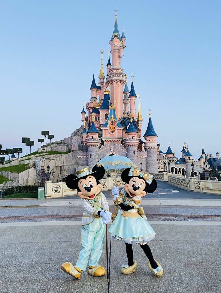 two mickey and minnie mouse statues in front of a castle