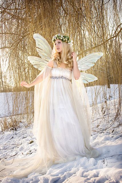 a woman dressed as a fairy standing in the snow wearing a white dress and holding her hands out