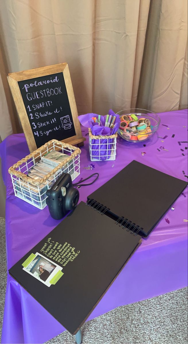 a purple table topped with lots of books and other items next to a chalkboard