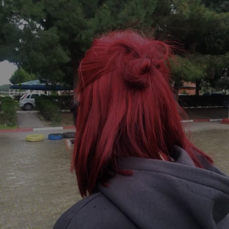 a woman with bright red hair is looking at something in the distance while wearing a gray jacket