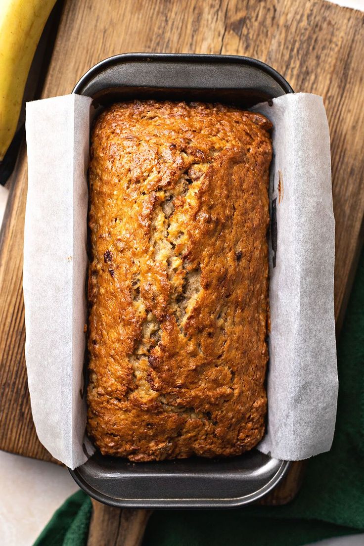 a loaf of banana bread sitting on top of a cutting board next to a banana