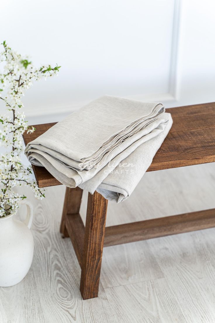 a white vase with flowers sitting on top of a wooden bench next to a table