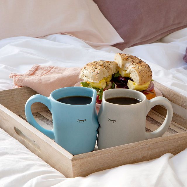 two cups of coffee sit on a tray next to a bagel and another sandwich