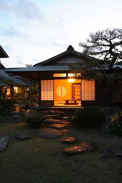 a small japanese house lit up by the sun in the evening with trees and rocks surrounding it