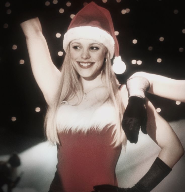 a woman wearing a santa hat and holding her arms in the air with both hands