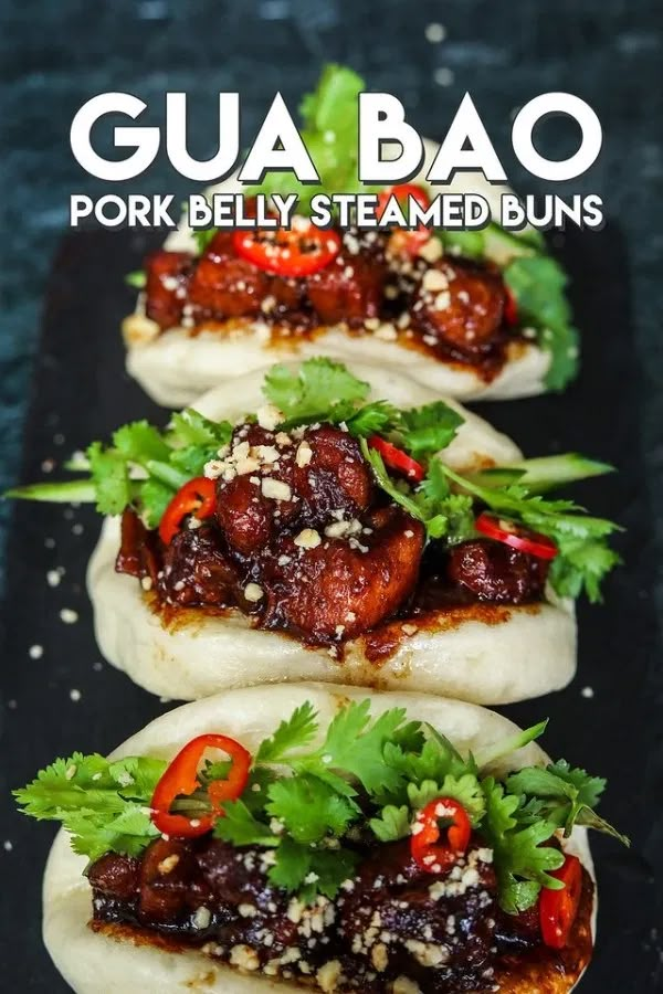 four pork belly steamed buns topped with cilantro and red peppers