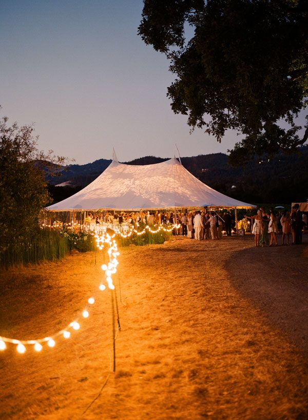 people are gathered under a tent at night with lights in the foreground and onlookers