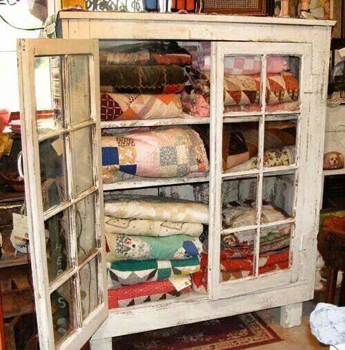 an old china cabinet is filled with quilts