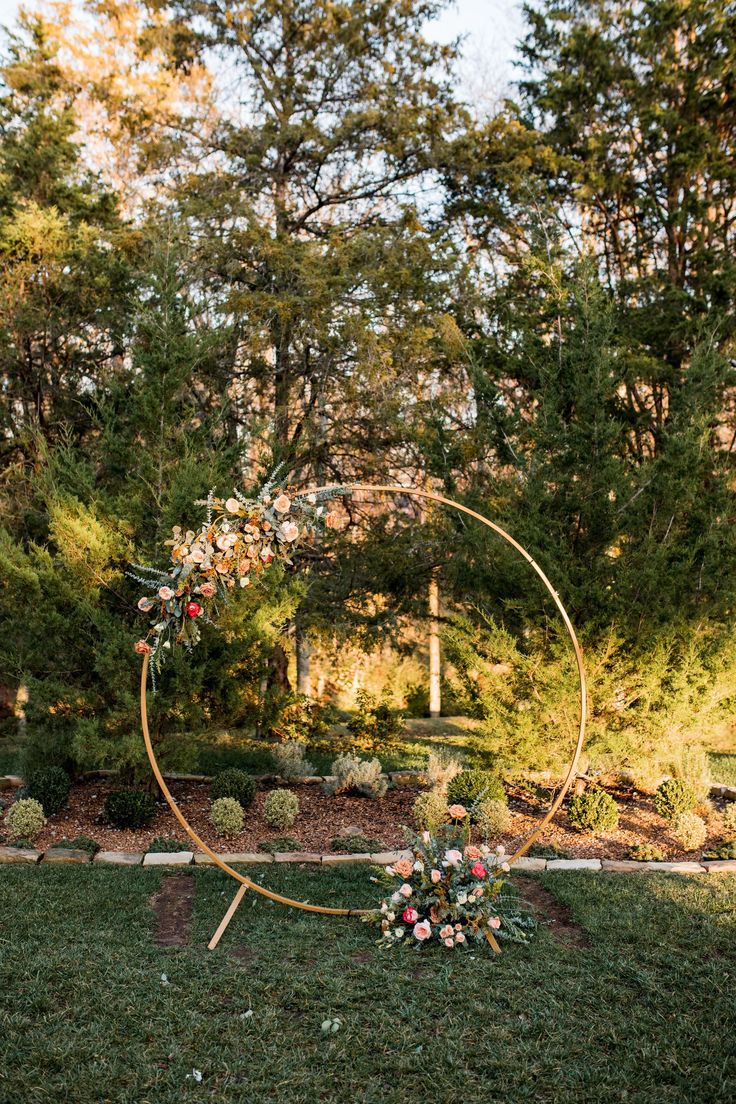 a wedding arch with flowers and greenery on the grass in front of some trees