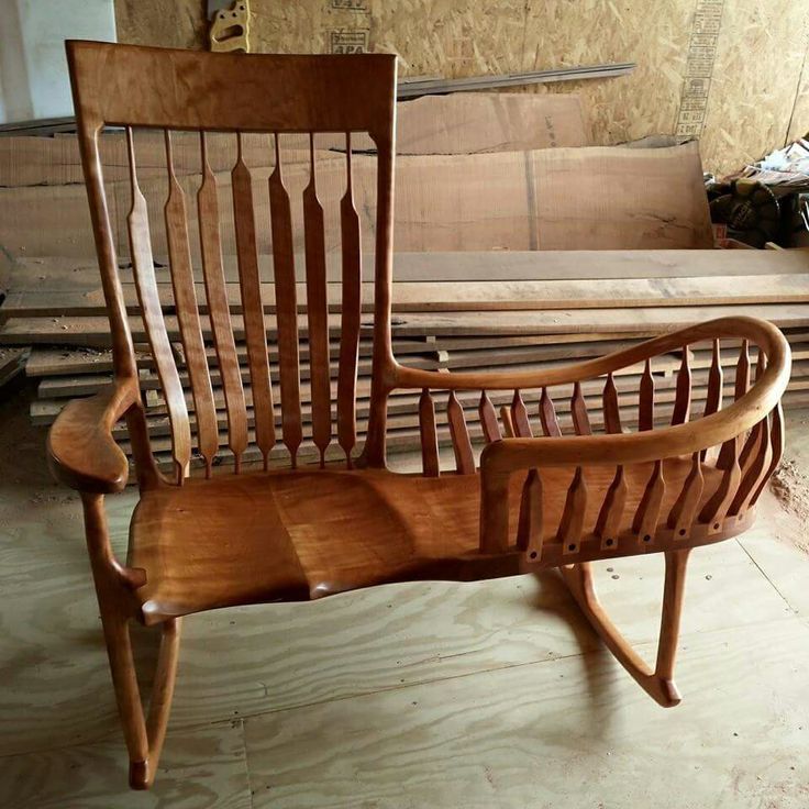 a wooden rocking chair sitting on top of a floor next to a pile of wood planks