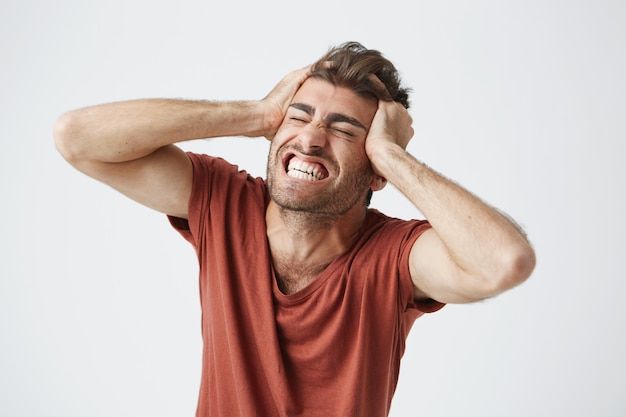 a man holding his head with one hand and smiling at the camera while standing against a white background