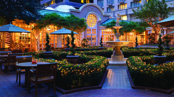 a courtyard with tables, chairs and lights in front of a large building at night