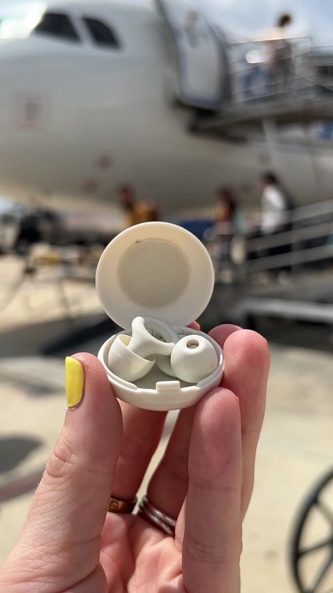 a hand holding an earbud in front of a plane on the tarmac