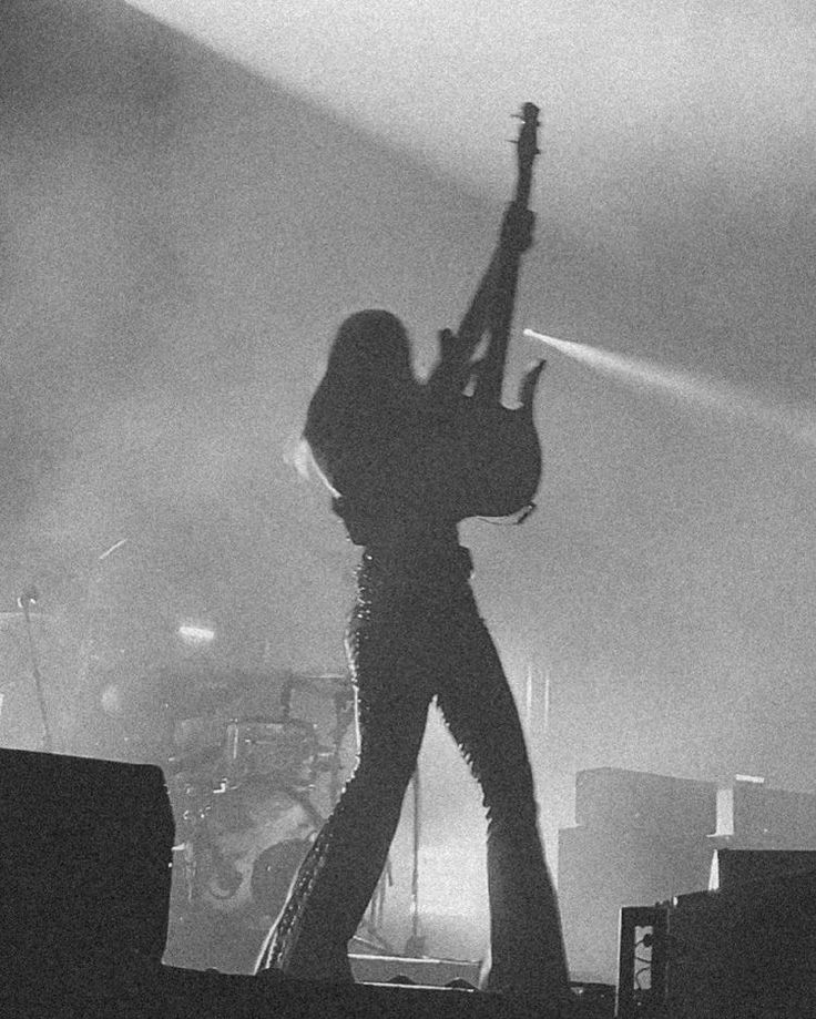 black and white photograph of a person on stage holding up a guitar in the air