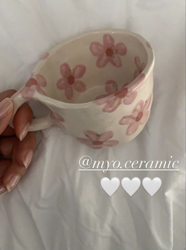 a woman's hand holding a cup with pink flowers on it