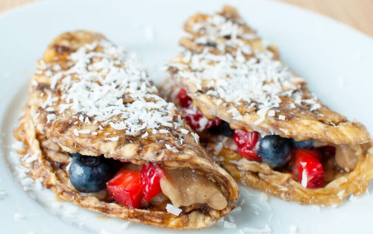 two crepes with fruit and powdered sugar on top sit on a white plate